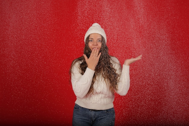 a happy girl in a winter hat and a knitted sweater in jeans on the background of artificial snow