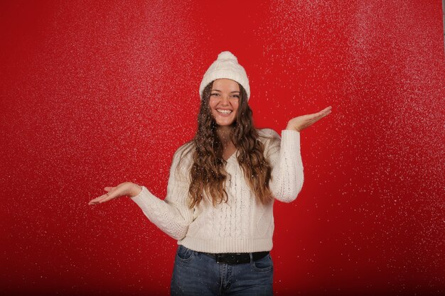 a happy girl in a winter hat and a knitted sweater in jeans on the background of artificial snow