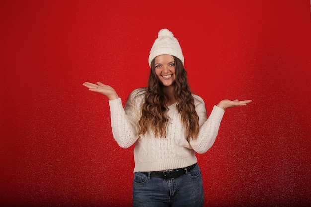 a happy girl in a winter hat and a knitted sweater in jeans on the background of artificial snow