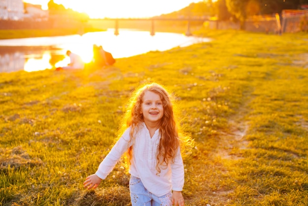 La ragazza felice con bei capelli ricci sorride mentre cammina intorno al fiume al tramonto