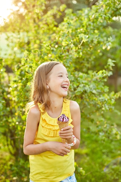 여름날 공원에서 쉬면서 웃고 있는 이탈리아 아이스크림 콘을 먹는 중괄호를 가진 행복한 소녀