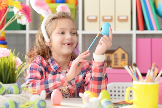 토끼 귀를 가진 행복한 소녀가 부활절을 준비하고 달걀을 색칠합니다.