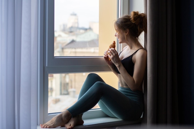 Ragazza felice con un croissant in una tuta da ginnastica ragazza dopo l'allenamento la ragazza ride la ragazza sta mangiando