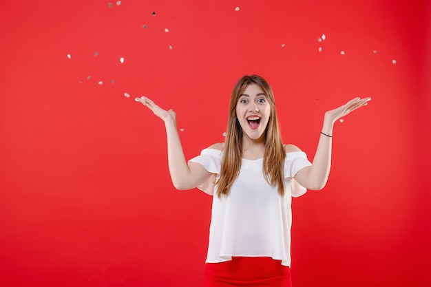 Happy girl with hearts confetti in the air isolated over red