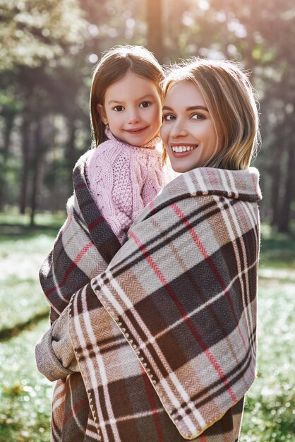 Happy girl with her beautiful mother in forest are covered with blanket