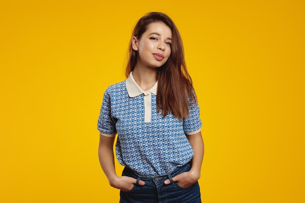 Happy girl with joyful expression smiling while standing in relaxed pose against yellow background