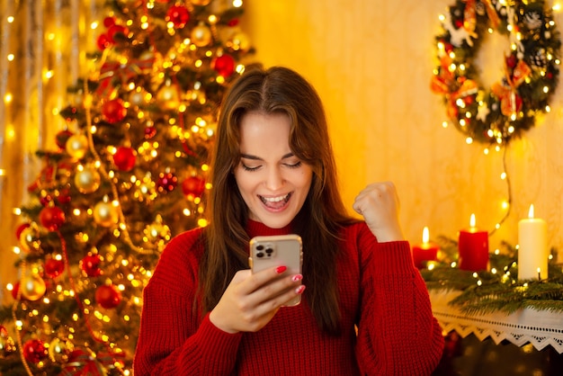 Счастливая девушка с телефоном в руках взволнована из-за сообщения в онлайн-чате, время поздравлений с Новым годом для семьи и друзей