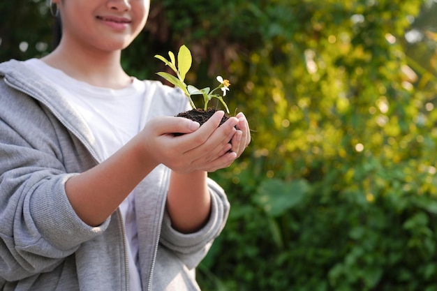 ぼやけた緑の自然の背景と彼女の手に植物を持つ幸せな女の子地球の日の環境の概念