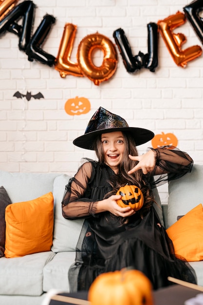 Foto ragazza felice con la zucca sul divano di casa concetto di vacanza di halloween e ottobre infanzia