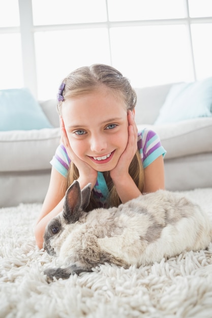Happy girl with rabbit lying on rug in living room