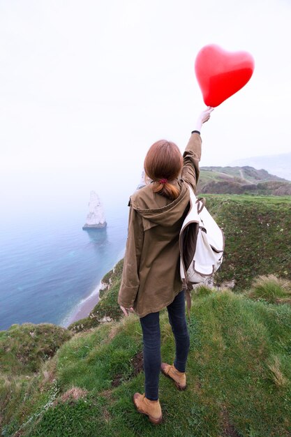 Happy girl with a red balloon in the shape of a heart at background of scenery Etretat. northern coast of France