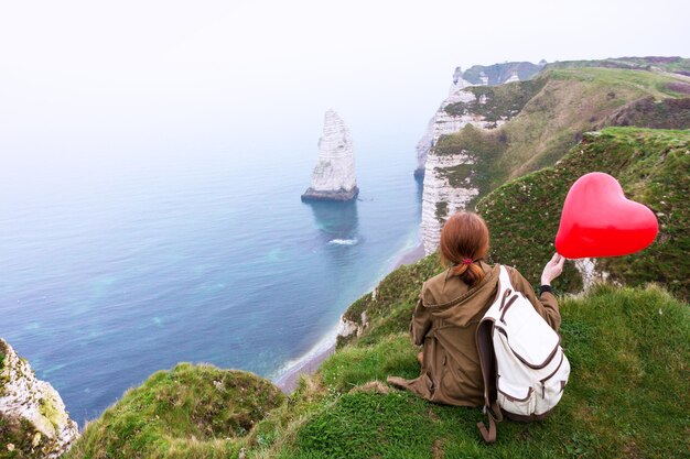 Happy girl with a red balloon in the shape of a heart at background of scenery Etretat. northern coast of France