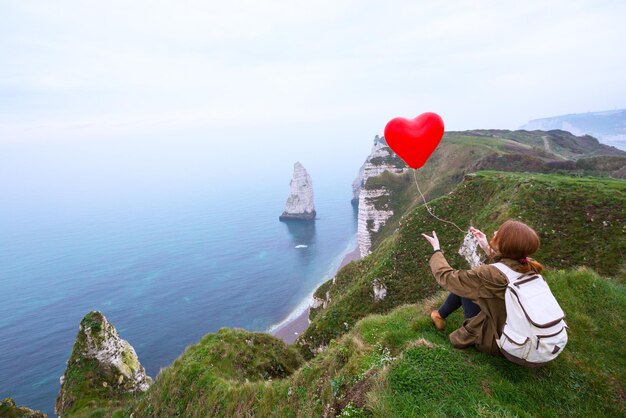 Happy girl with a red balloon in the shape of a heart at background of scenery Etretat. northern coast of France