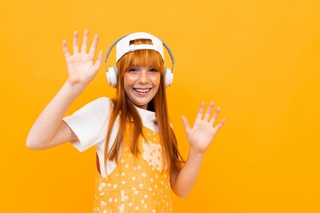 Happy girl with red hair listen to music with big white earphones and smiles with isolated on yellow background