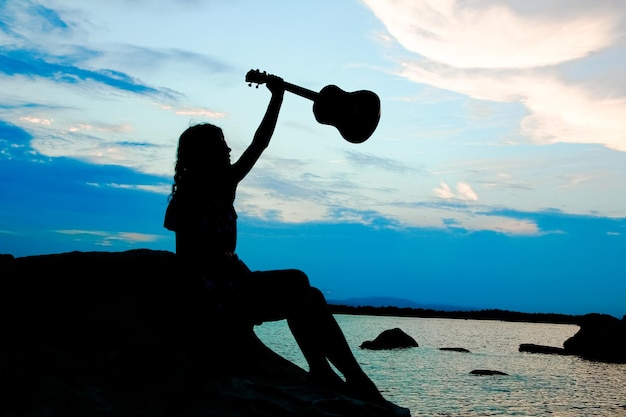 Happy girl with ukulele by the sea on nature silhouette background