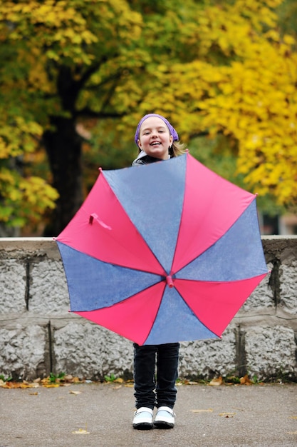 秋の季節の雨の日に公園で屋外の傘を持つ幸せな女の子