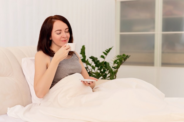 Happy girl woman drink coffee on the bed.