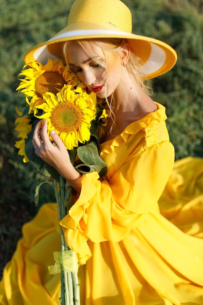 happy girl in a yellow dress holds sunflower flowers in a field of sunflowers against the sky