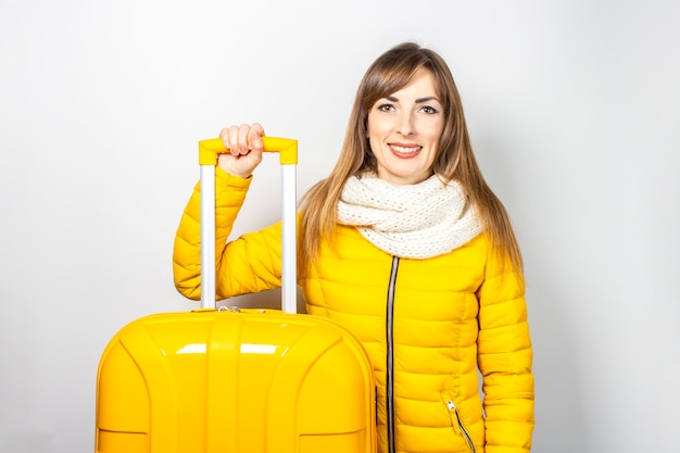 Happy girl in a yellow jacket holds the handle of a yellow suitcase