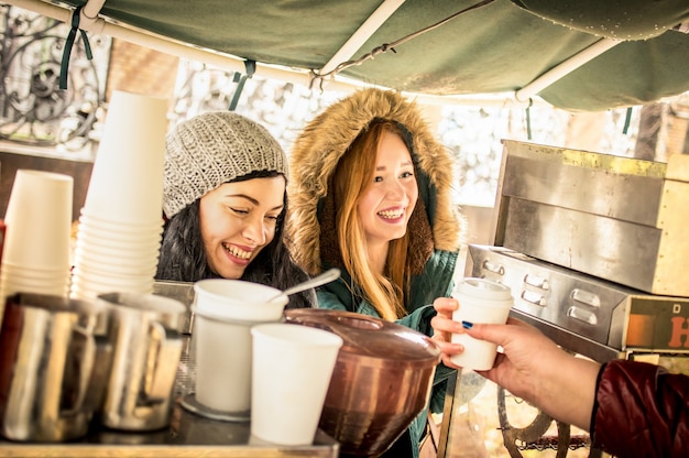 Happy girlfriends best friends sharing time together outdoors at coffee takeaway vendor