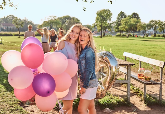 Happy girlfriends posing with balloons near a table celebrating a birthday at the outdoor park.