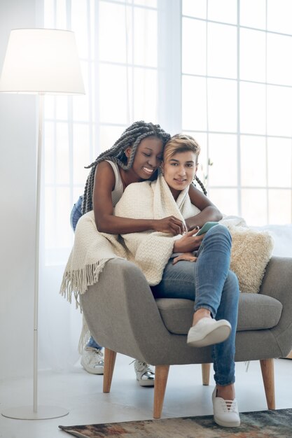 Happy girls. African american smiling girl hugging her girlfriend sitting in the chair