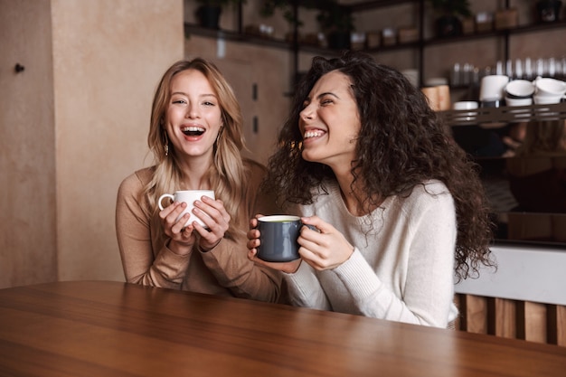 a happy girls friends sitting in cafe talking with each other drinking tea or coffee