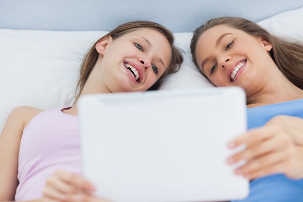 Happy girls lying in bed holding tablet