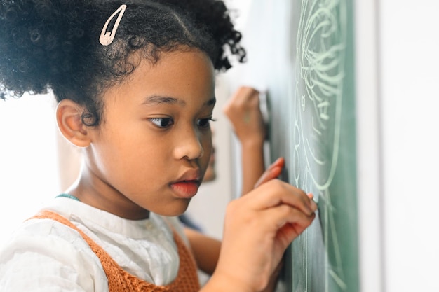 Happy girls pupils writing on blackboard in classroom at elementary school Students doing test