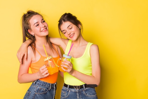 Happy girls smiling with drinks on yellow background