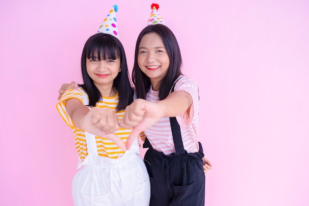 Happy girls wear party hat palying on pink background.