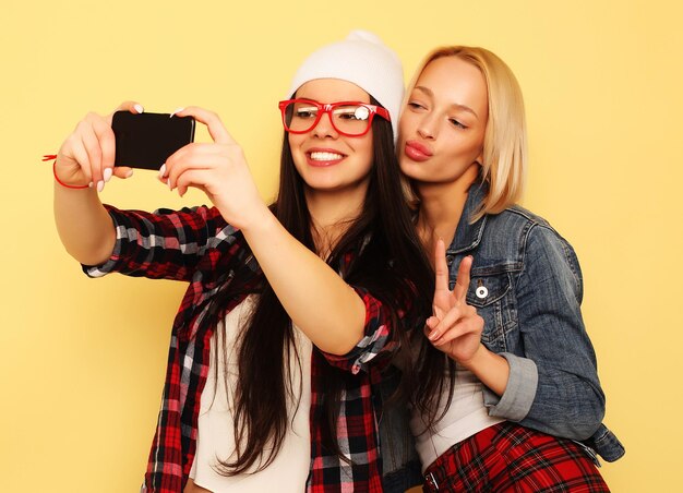 Happy girls with smartphone over yellow background Happy self