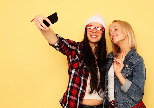 Счастливые девушки со смартфоном на желтом фоне