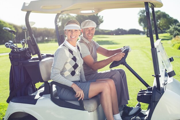 Happy golfing couple sitting in buggy smiling at camera