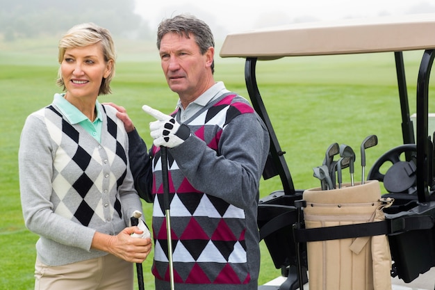 Photo happy golfing couple with golf buggy behind