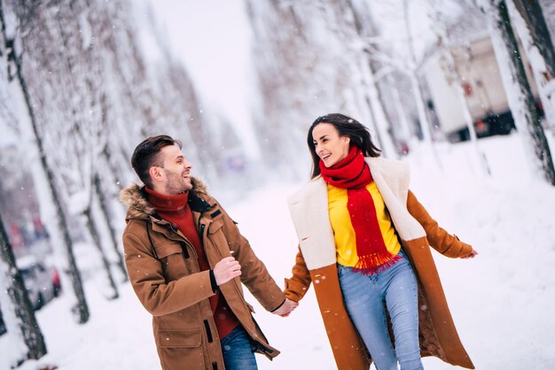 愛する人との幸せで良い一日。恋に興奮した若いカップルが冬の都市公園で一緒に歩いて楽しんでいます
