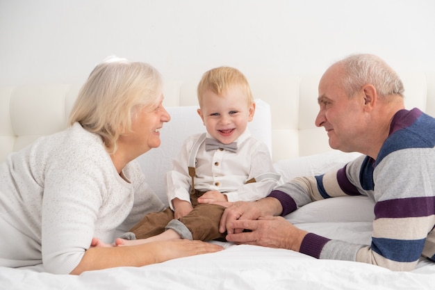 Счастливый красивый старший пара муж и жена с их очаровательным внуком на кровати.