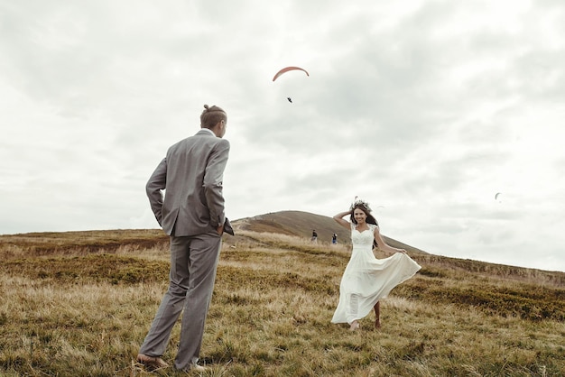 Foto felice splendida sposa che corre dallo sposo e si diverte a una cerimonia di lusso in montagna con uno spazio di vista incredibile per gli sposi boho del testo