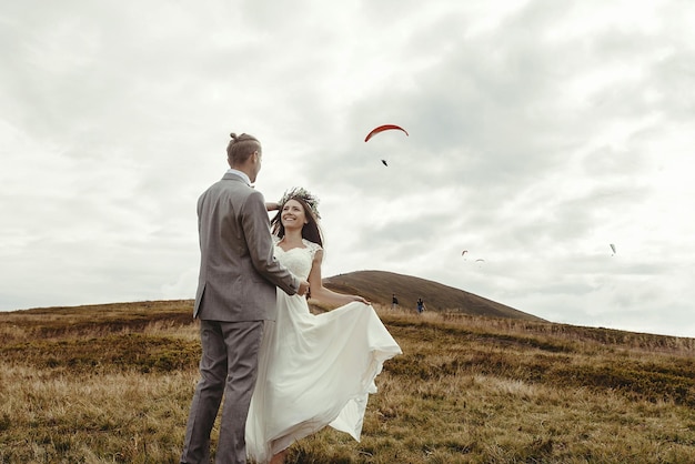 Foto felice splendida sposa che corre dallo sposo e si diverte a una cerimonia di lusso in montagna con uno spazio di vista incredibile per gli sposi boho del testo