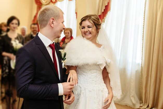 Счастливая великолепная невеста и стильный жених обмениваются обручальными кольцами и смеются над эмоциональным моментом официальной церемонии