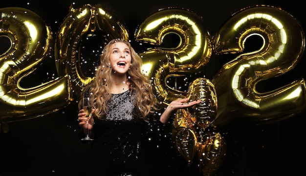 Happy gorgeous girl in stylish sexy party dress holding gold 2022 balloons, having fun at Christmas or New Year's Eve Party.