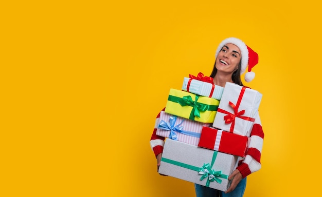 Happy gorgeous woman with many Christmas and New year presents in hands is posing on yellow background