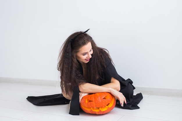 Happy gothic young woman in witch halloween costume smiling over white room surface