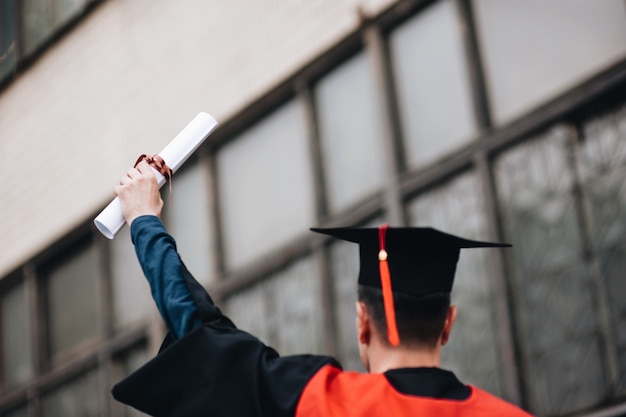 Foto felice laureato in abito regge un diploma di laurea