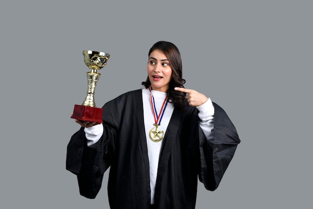 Foto ragazza felice dello studente laureato che tiene il trofeo d'oro che punta con il modello pakistano indiano del dito