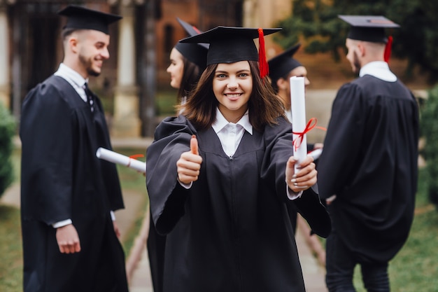 Happy graduates Masters graduates standing in a row and turns up finger