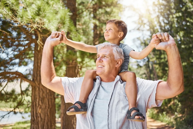 Foto felice nonno bambino e ritorno nella foresta per un viaggio o un legame familiare insieme all'aperto il nonno sorride portando il bambino sulle spalle per un viaggio avventuroso o un viaggio nella natura o nei boschi