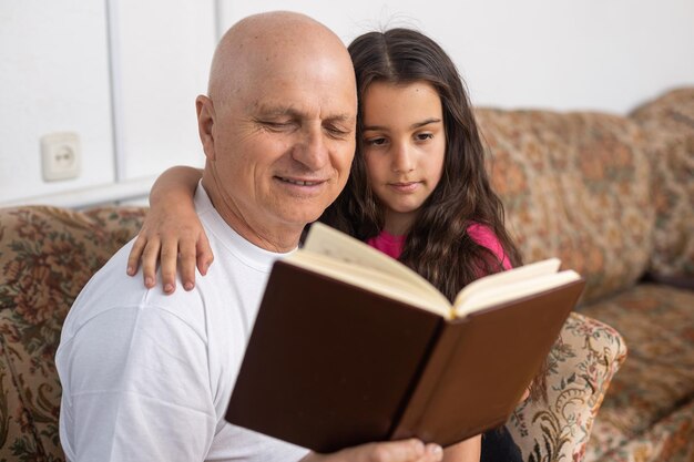 Happy grandfather and granddaughter reading book together at home. Close up.