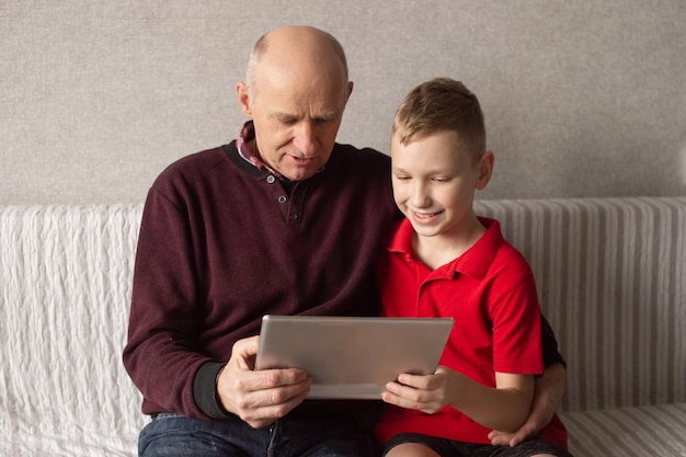 Happy grandfather and grandson look into the gadget and hug