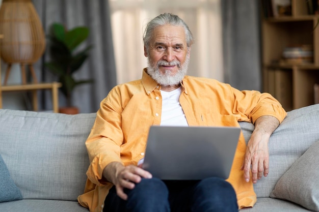 Happy grandfather websurfing while resting at home using laptop